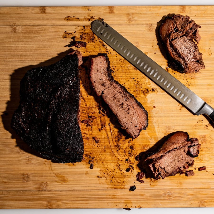 Poitrine de bœuf fumée entière et ses premières tranches, sur une planche.