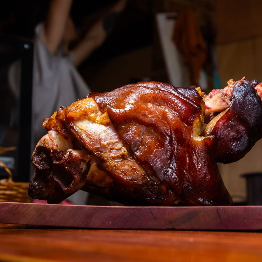 Jarret de porc confit, la couenne dorée, posé sur une planche.