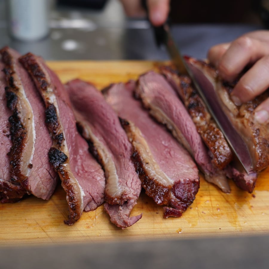 Pièce de bœuf fumée tranchée au couteau, en éventail sur la planche.